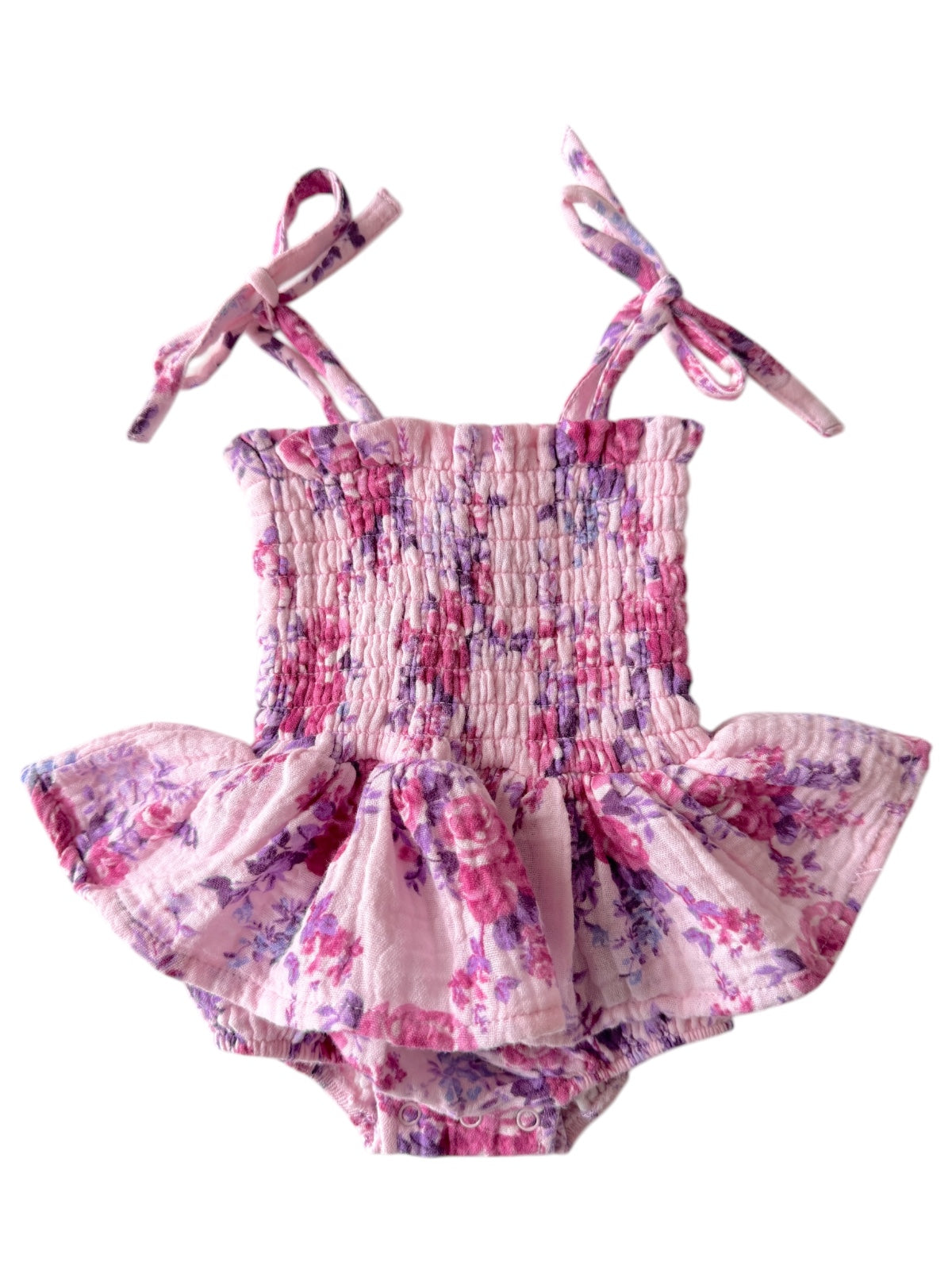 Floral patterned pink baby romper with smocked top and ruffled skirt, featuring adjustable tie straps.
