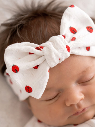 Newborn with a white headband featuring red ladybug patterns, peacefully sleeping.