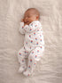 Sleeping baby in a white onesie with colorful patterns, nestled on a soft, light-colored blanket.
