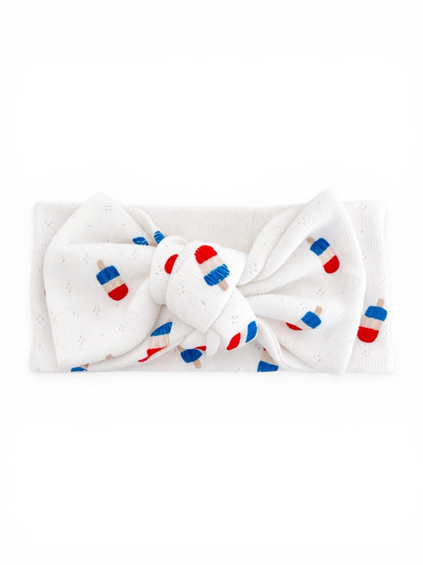 White headband with a large bow featuring red and blue ice pop patterns.