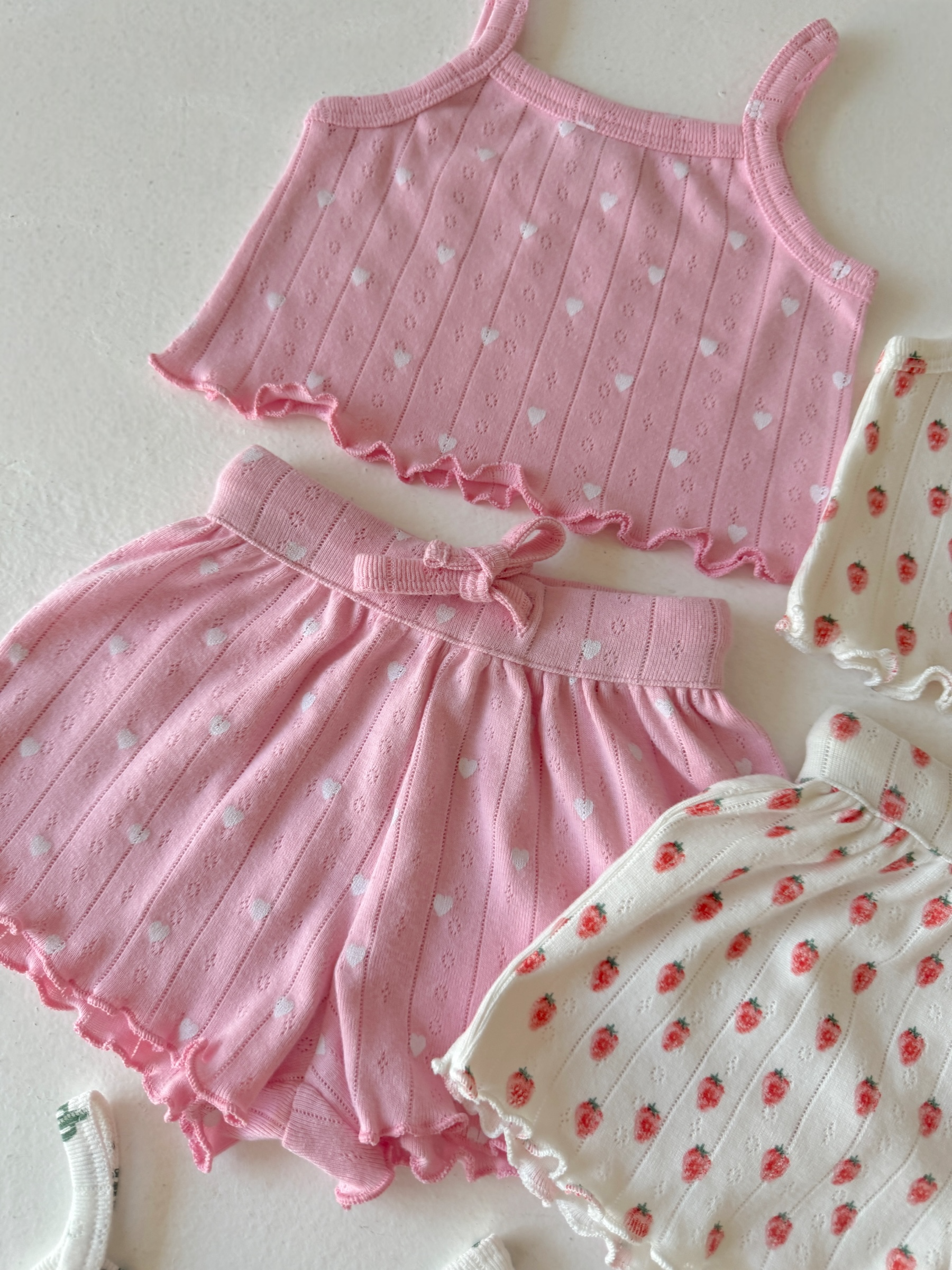Pink heart-patterned crop top and matching shorts, alongside a white floral-patterned outfit.