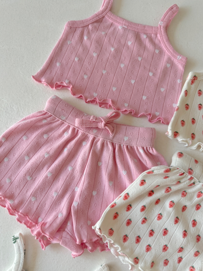 Pink heart-patterned crop top and matching shorts, alongside a white floral-patterned outfit.