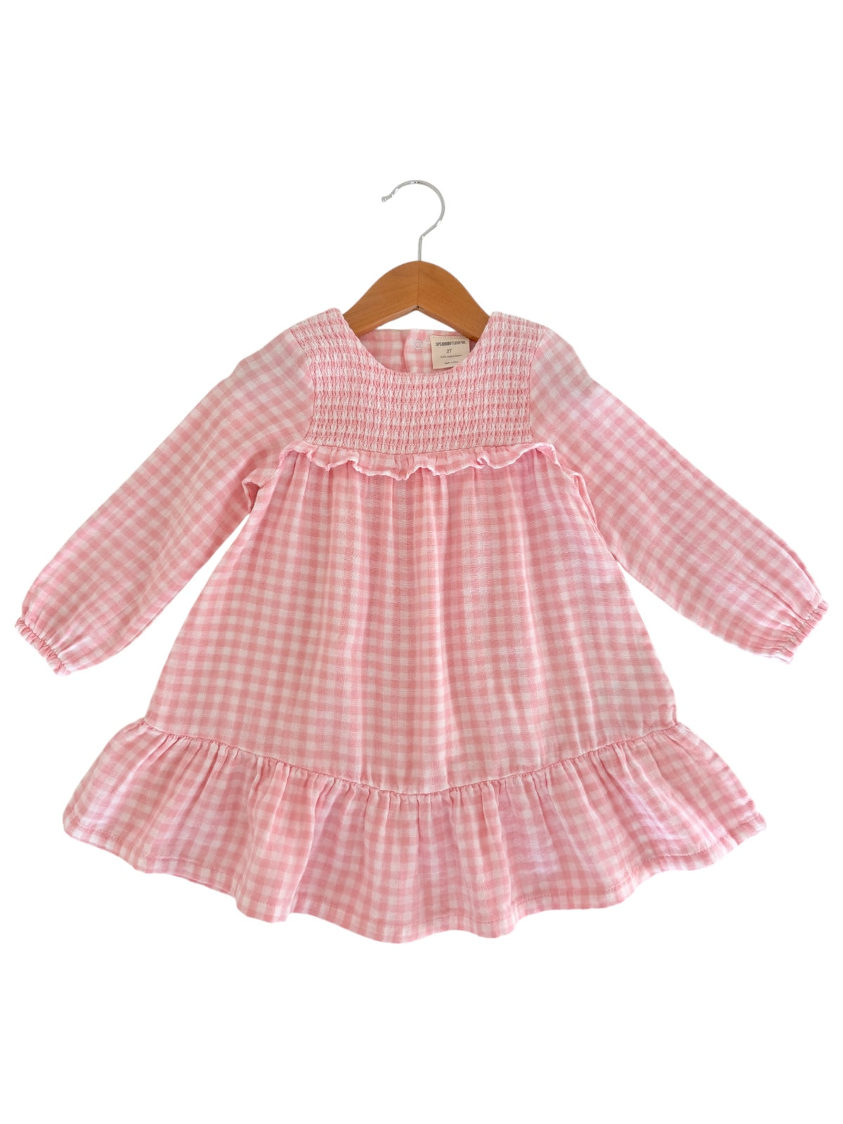 Pink gingham dress with long sleeves and ruffled hem, displayed on a wooden hanger.
