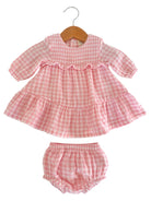 Pink gingham dress with matching bloomers hanging on a wooden hanger. Perfect for young children.