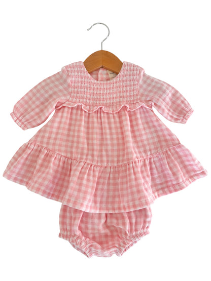 Pink gingham dress with long sleeves and ruffled hem, hung on a wooden hanger. Includes matching bloomer bottom.