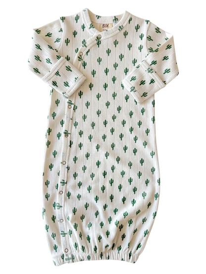 White baby outfit adorned with green cactus prints, featuring snaps along the side and gathered bottom for comfort.