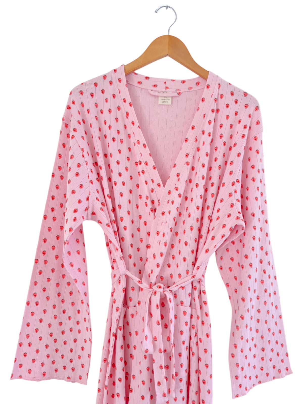 Pink robe with strawberry pattern, featuring long sleeves and a waist tie, hanging on a wooden hanger.