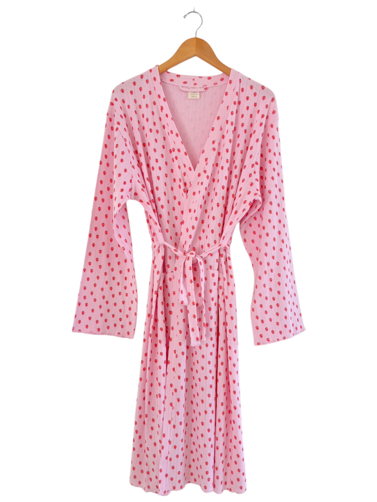 Pink robe with red polka dots, featuring long sleeves and a tied waist, hanging on a wooden hanger.