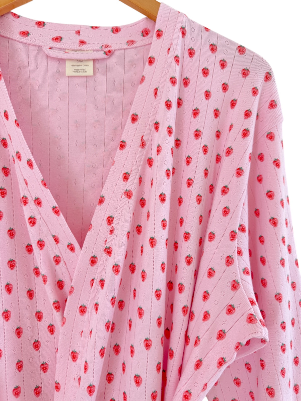 Pink robe with small red strawberry patterns, showcased on a wooden hanger.