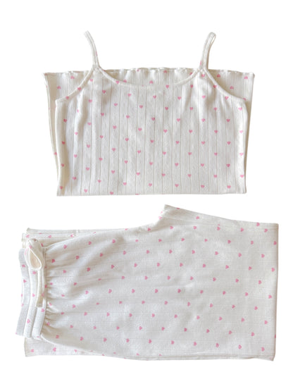 White pajama set featuring a spaghetti strap top and pants with pink heart patterns. Perfect for cozy nights.