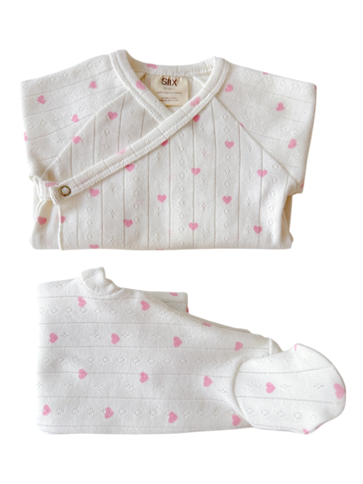 White baby outfit featuring pink heart patterns, including a top, pants, and hat.