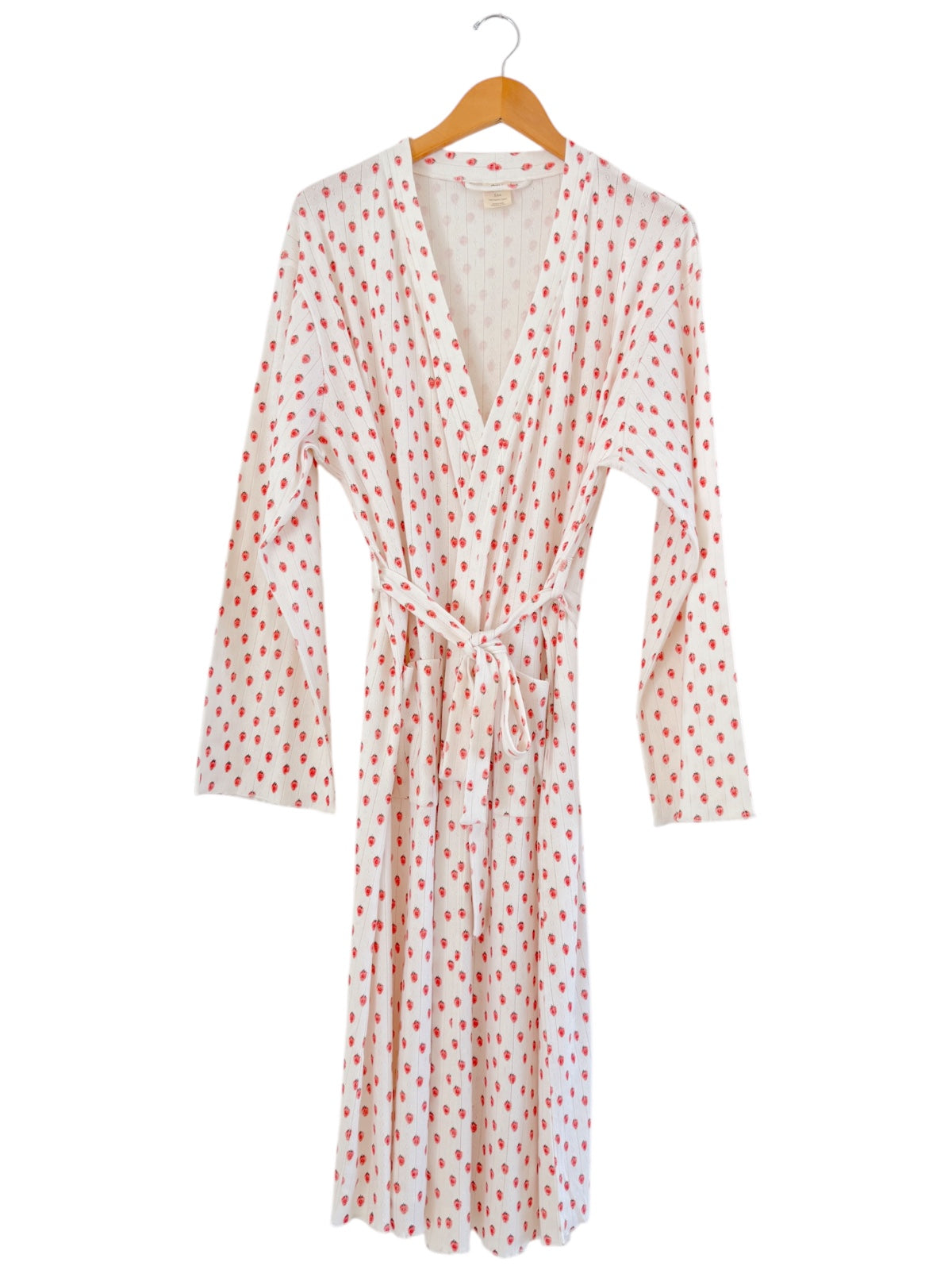 White robe with red polka dots, long sleeves, and a tied waist, displayed on a wooden hanger.