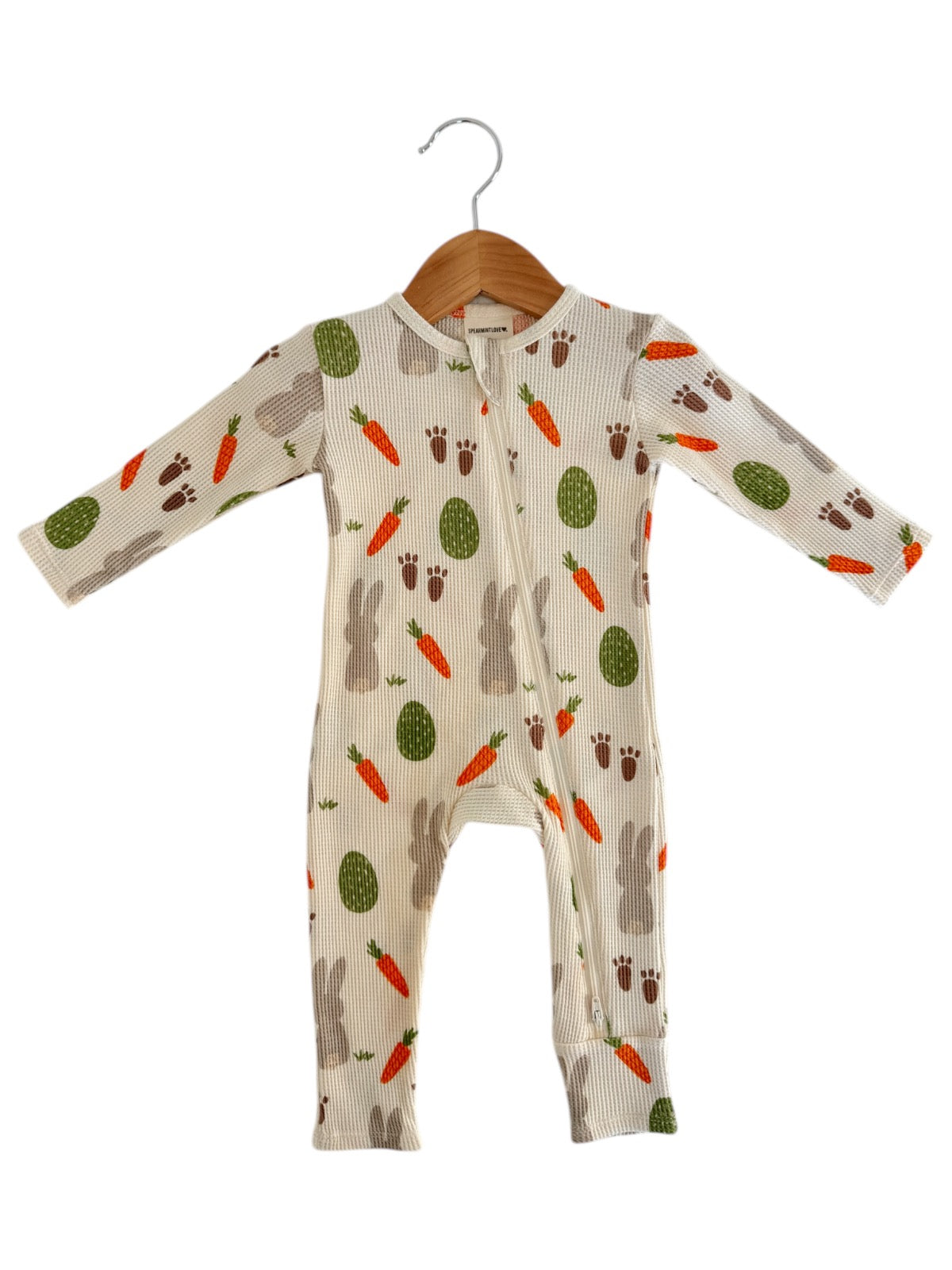 Baby onesie with bunny, carrot, and egg pattern on a light background, hanging on a wooden hanger.