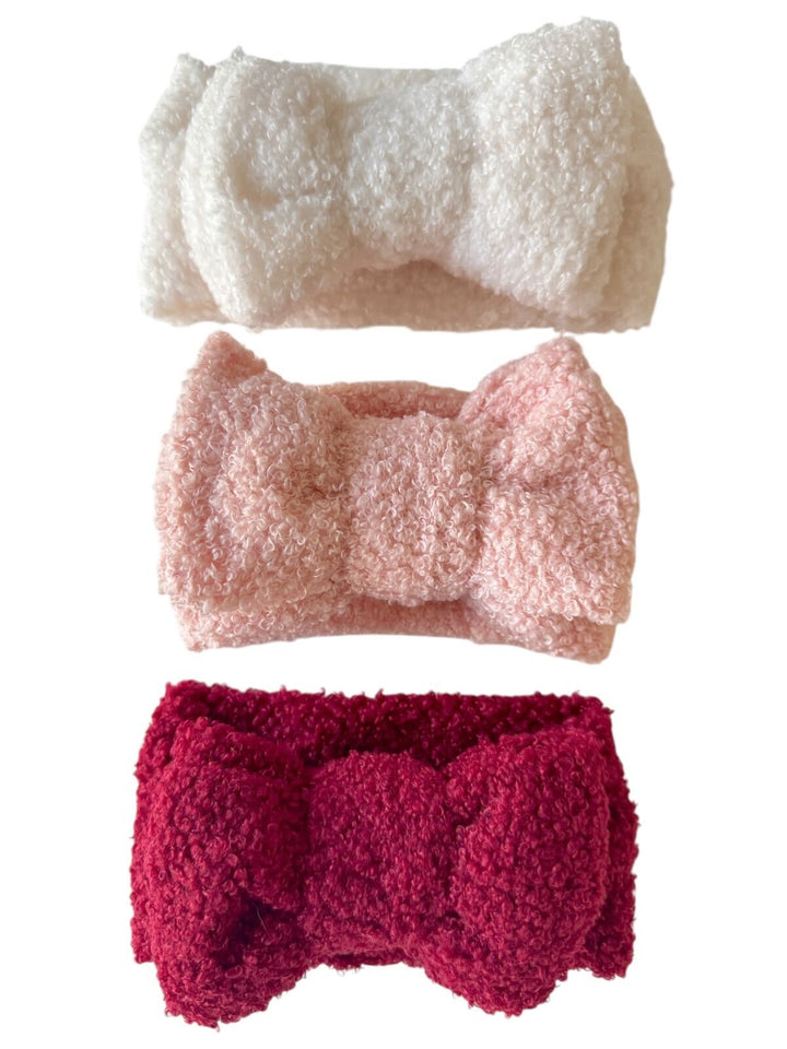 Three fluffy hairbands in white, pink, and burgundy stacked vertically, each adorned with a bow.