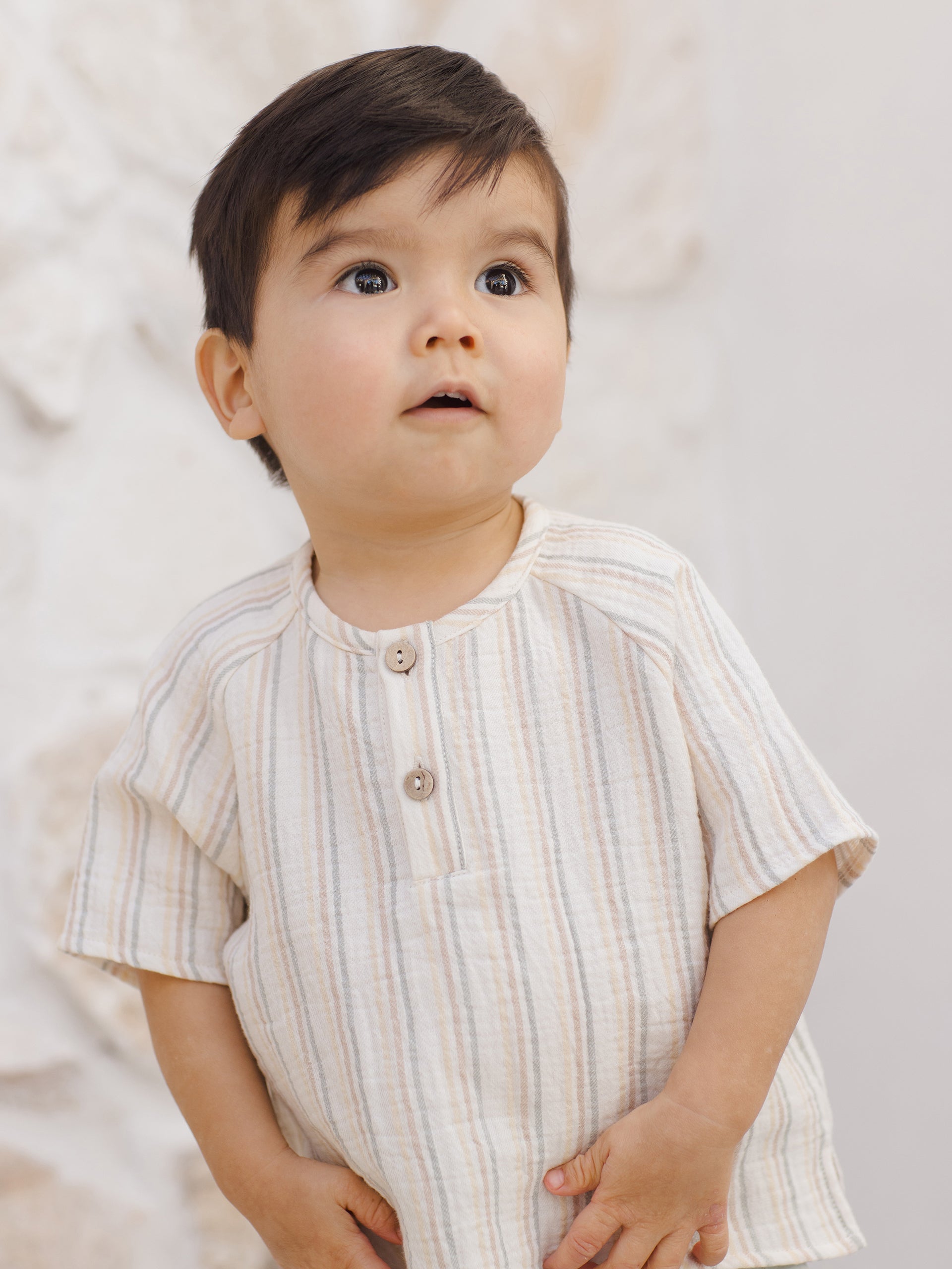 Young child with short hair, wearing a striped shirt, gazing upward against a light background.