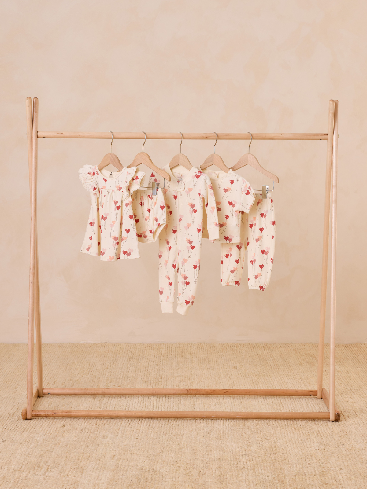 Children's clothing with heart patterns displayed on a wooden rack against a neutral background.