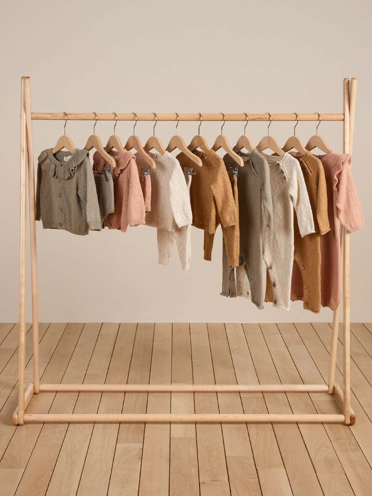 Collection of knit cardigans in various colors displayed on a wooden hanger against a neutral background.