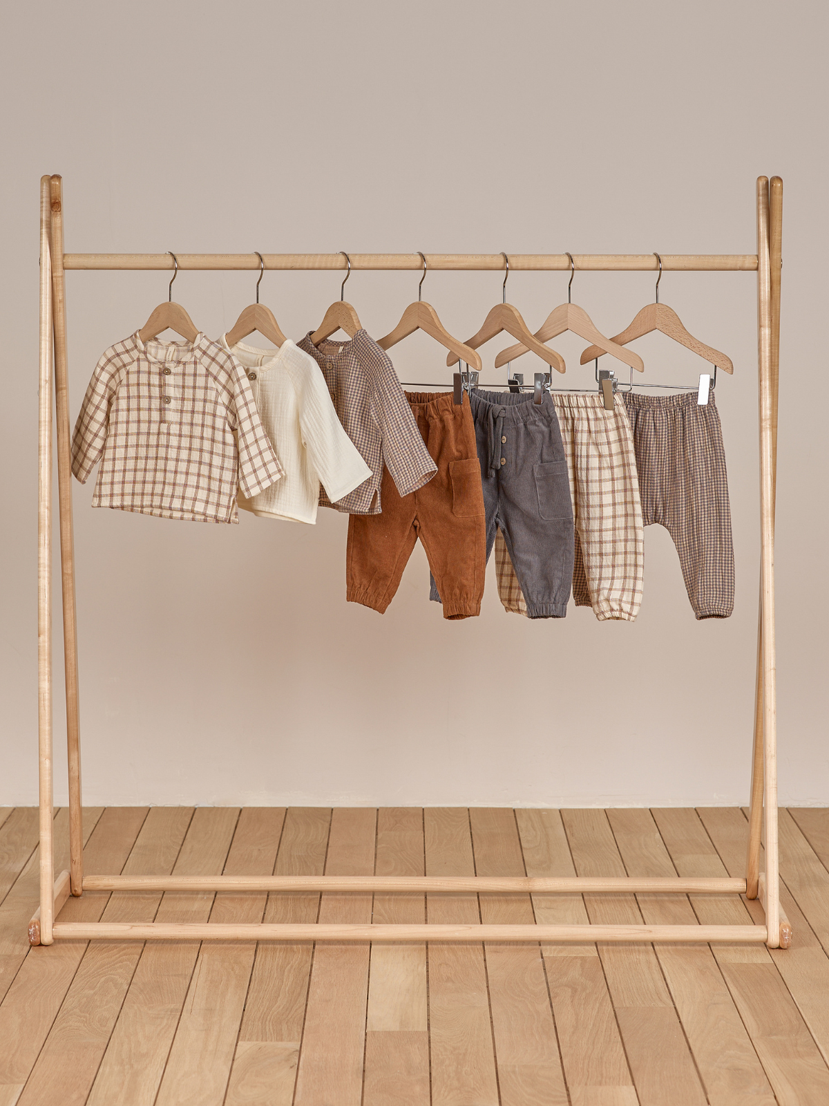 Children's clothing displayed on a wooden rack, featuring various tops and pants in neutral colors and patterns.
