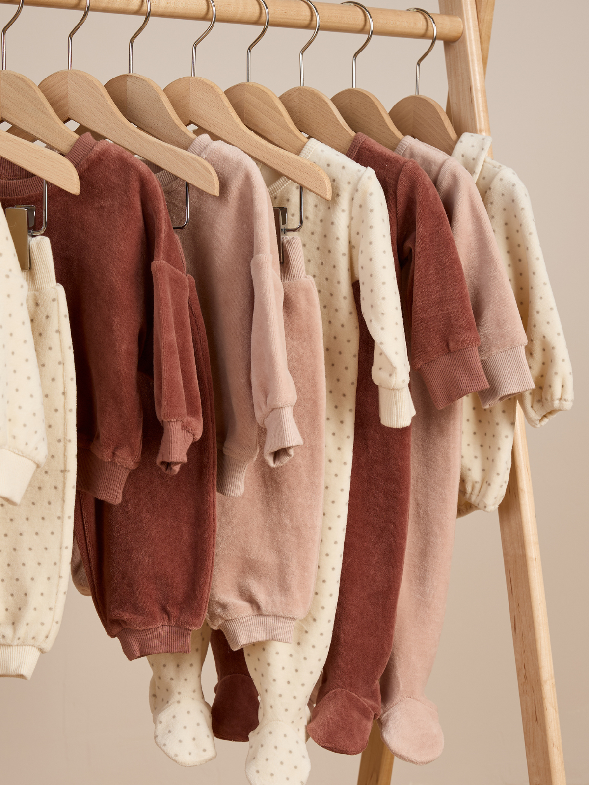 Hanging baby onesies in soft colors, featuring polka dots, on wooden hangers against a neutral background.