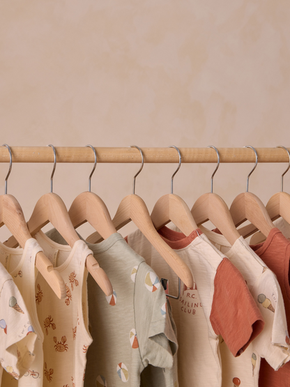 Assorted children’s shirts hanging on wooden hangers against a soft, neutral background.