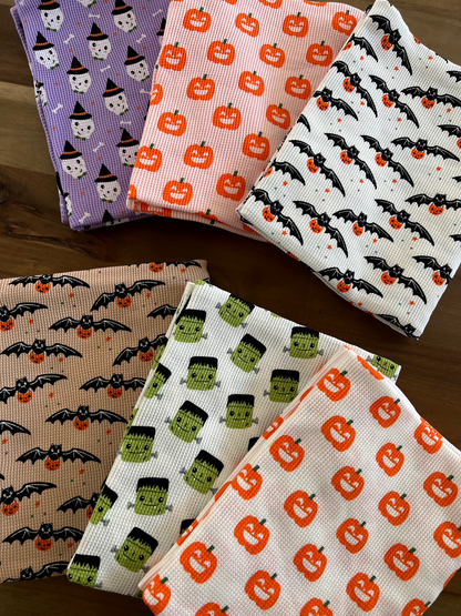 Colorful Halloween-themed fabrics featuring pumpkins, ghosts, bats, and Frankenstein designs stacked on a wooden surface.
