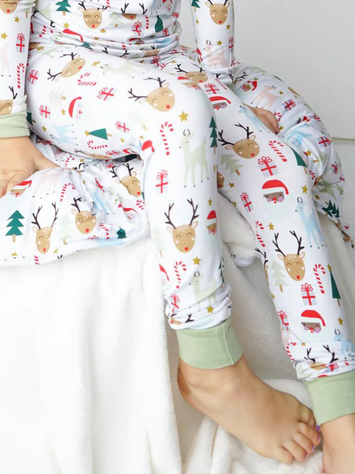 Child wearing festive pajamas with reindeer and holiday patterns, seated on a cozy blanket.