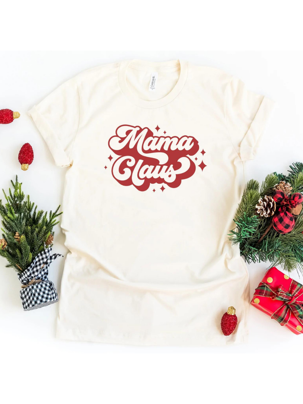 Cream t-shirt with red "Mama Claus" text, surrounded by holiday decorations and gifts.