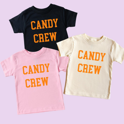 Three T-shirts in pink, cream, and black, all with "CANDY CREW" printed in orange on the front.