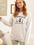 Woman smiling in a gray sweatshirt with "CottonTail Farms" and a bunny graphic, featuring green leggings.