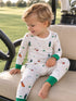 Toddler in golf-themed pajamas smiling while sitting on a golf cart seat, green grass in the background.