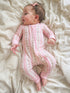 Baby girl in a pink floral onesie, lying on a cream-colored blanket, smiling with a small hair bow.