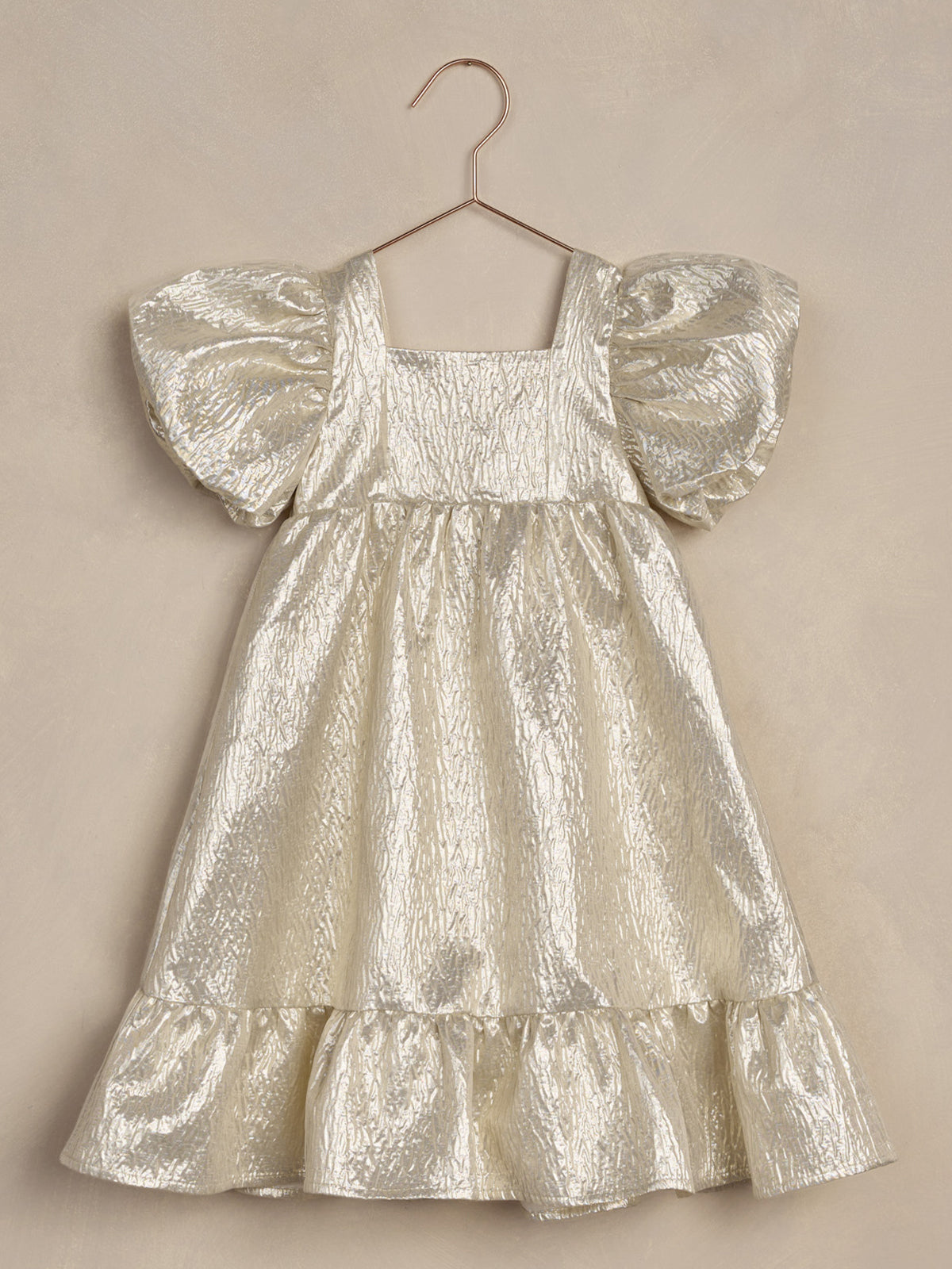 Shiny silver dress with puff sleeves and a ruffled hem, hanging on a hook against a textured background.