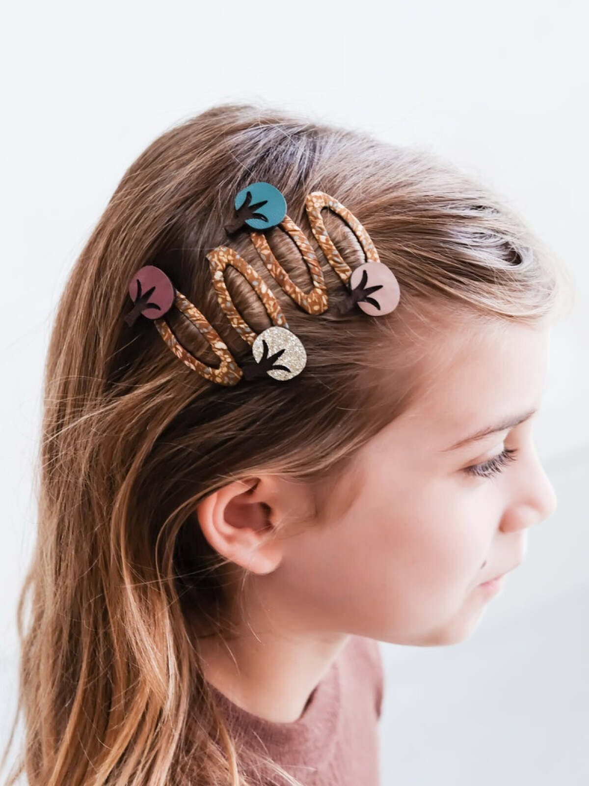 Child with hair clips in multiple colors, styled in wavy hair against a light background.