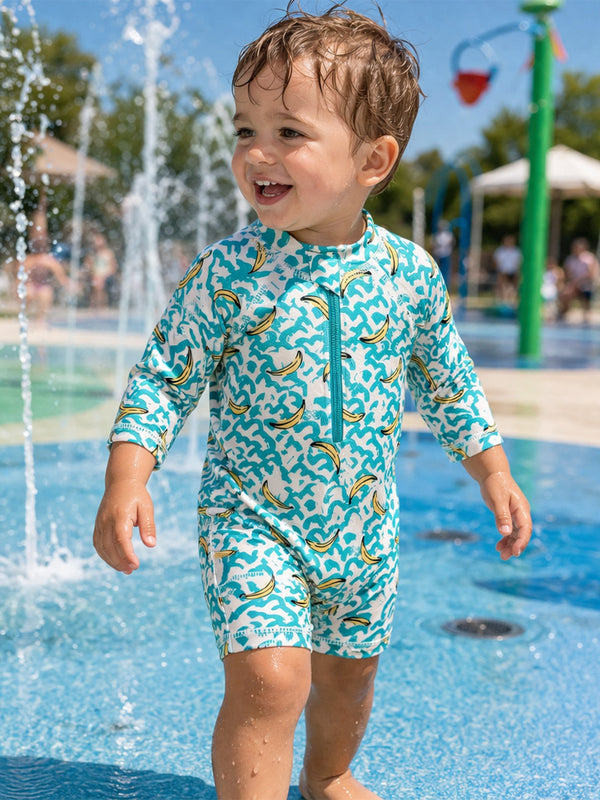 Smiling child in a colorful swimsuit playing in a splash pad, surrounded by water sprays on a sunny day.