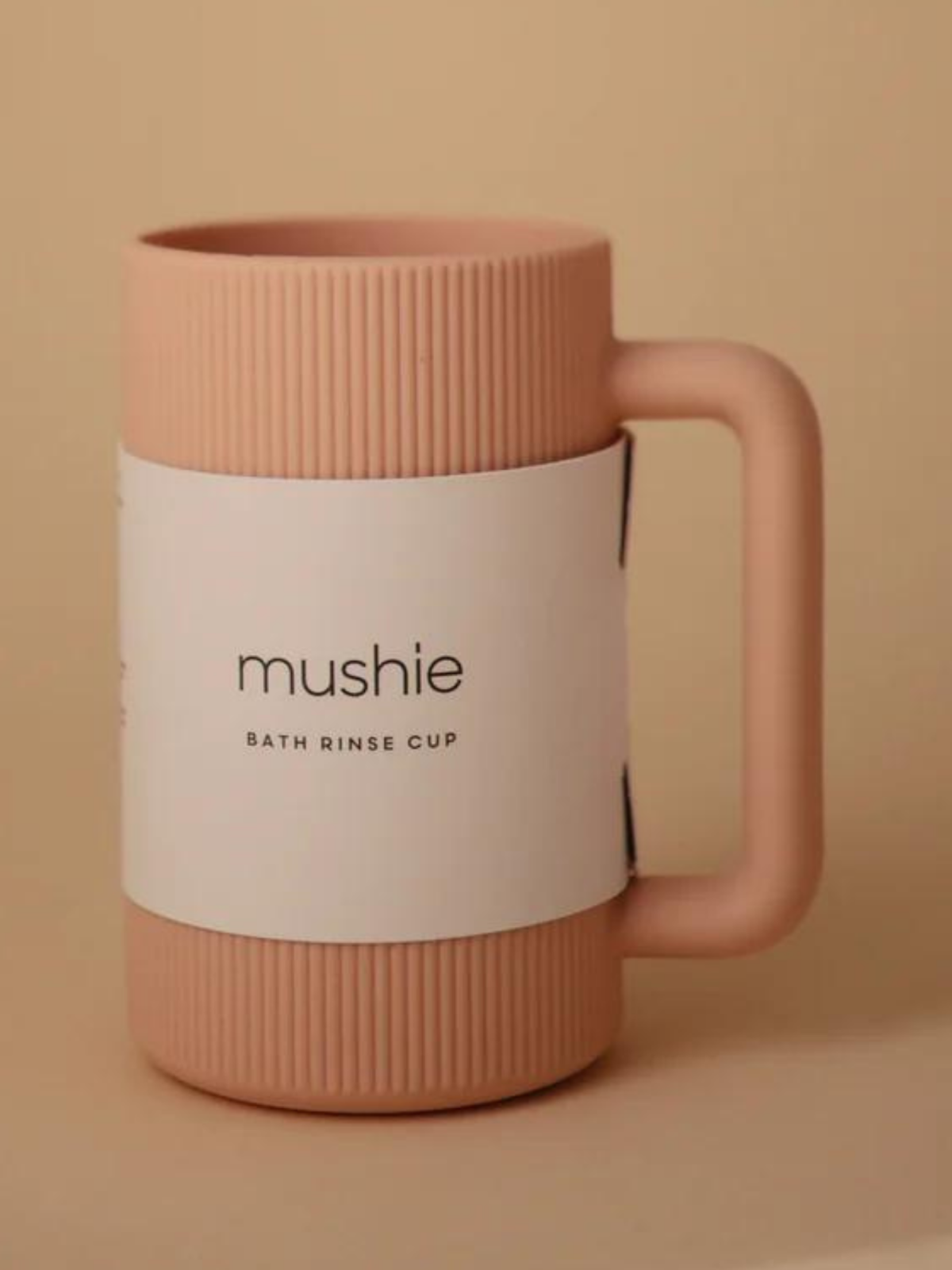 Pink bath rinse cup with ribbed design and label reading "mushie bath rinse cup".