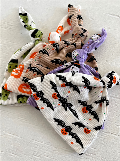 Three Halloween-themed baby hats with bat, pumpkin, and monster designs, tied at the top.