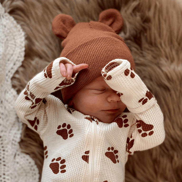 Newborn baby wearing a bear-themed hat and paws-printed outfit, peacefully resting on a cozy blanket.