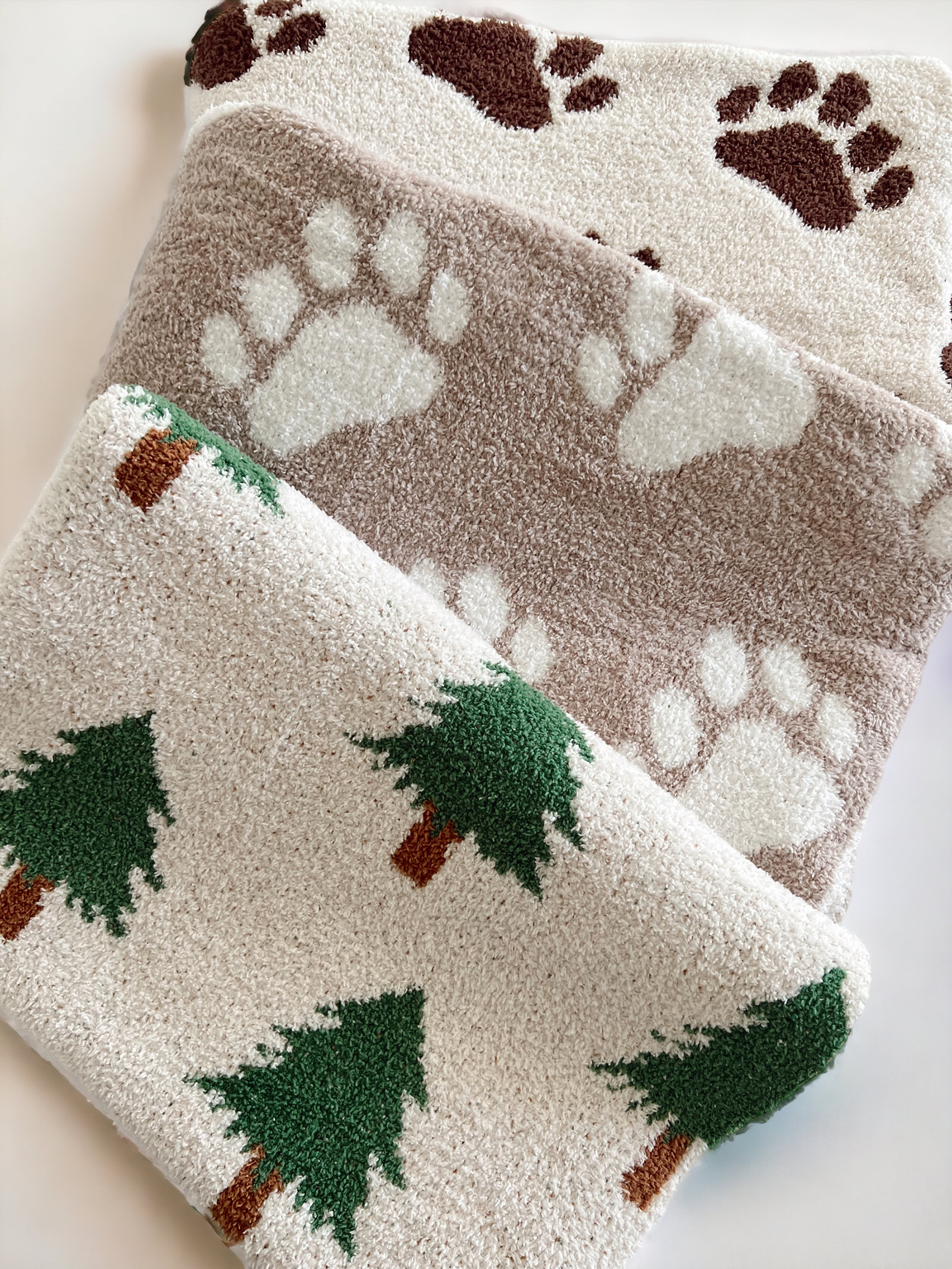 Three soft blankets with paw print and tree patterns in earthy tones. Perfect for pet lovers and nature enthusiasts.