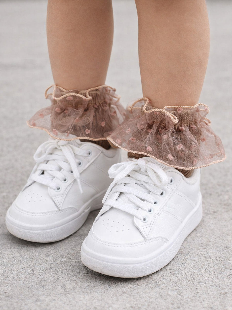 White sneakers with frilly, pink heart-patterned ankle socks on a child's feet.