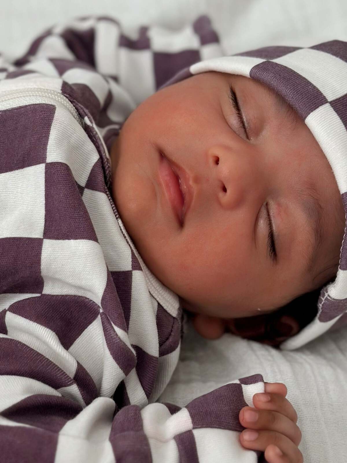 Sleeping baby in a purple and white checkered outfit, resting peacefully on a soft surface.