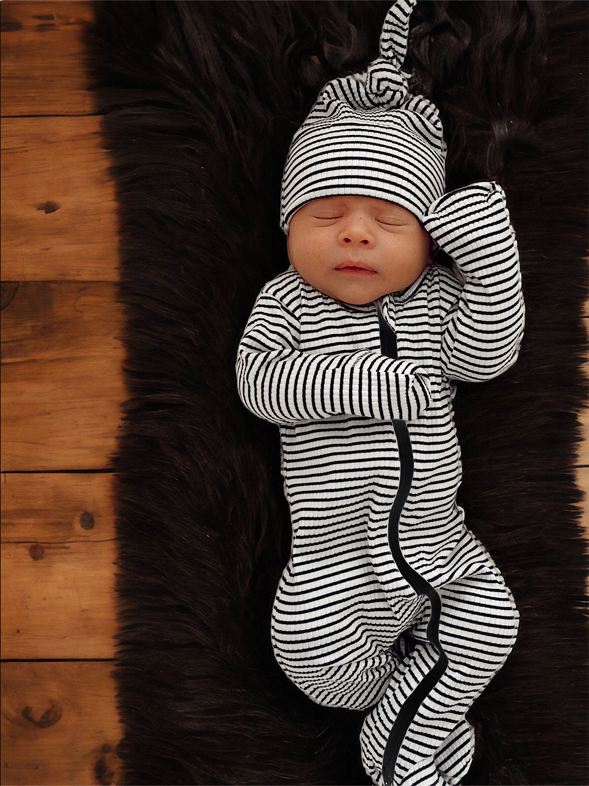 Newborn baby in striped pajamas sleeping peacefully on a soft fur rug.