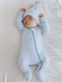 Infant sleeping peacefully in a blue and white striped onesie with a matching hat on a soft white surface.