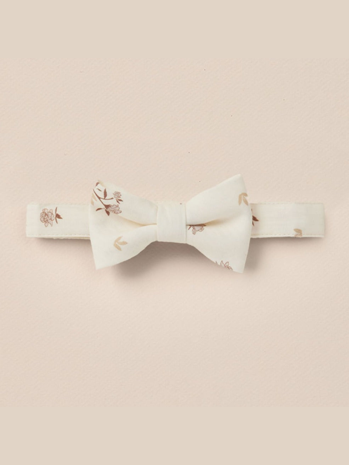 Floral-patterned bow tie in cream color, displayed against a soft pink background.