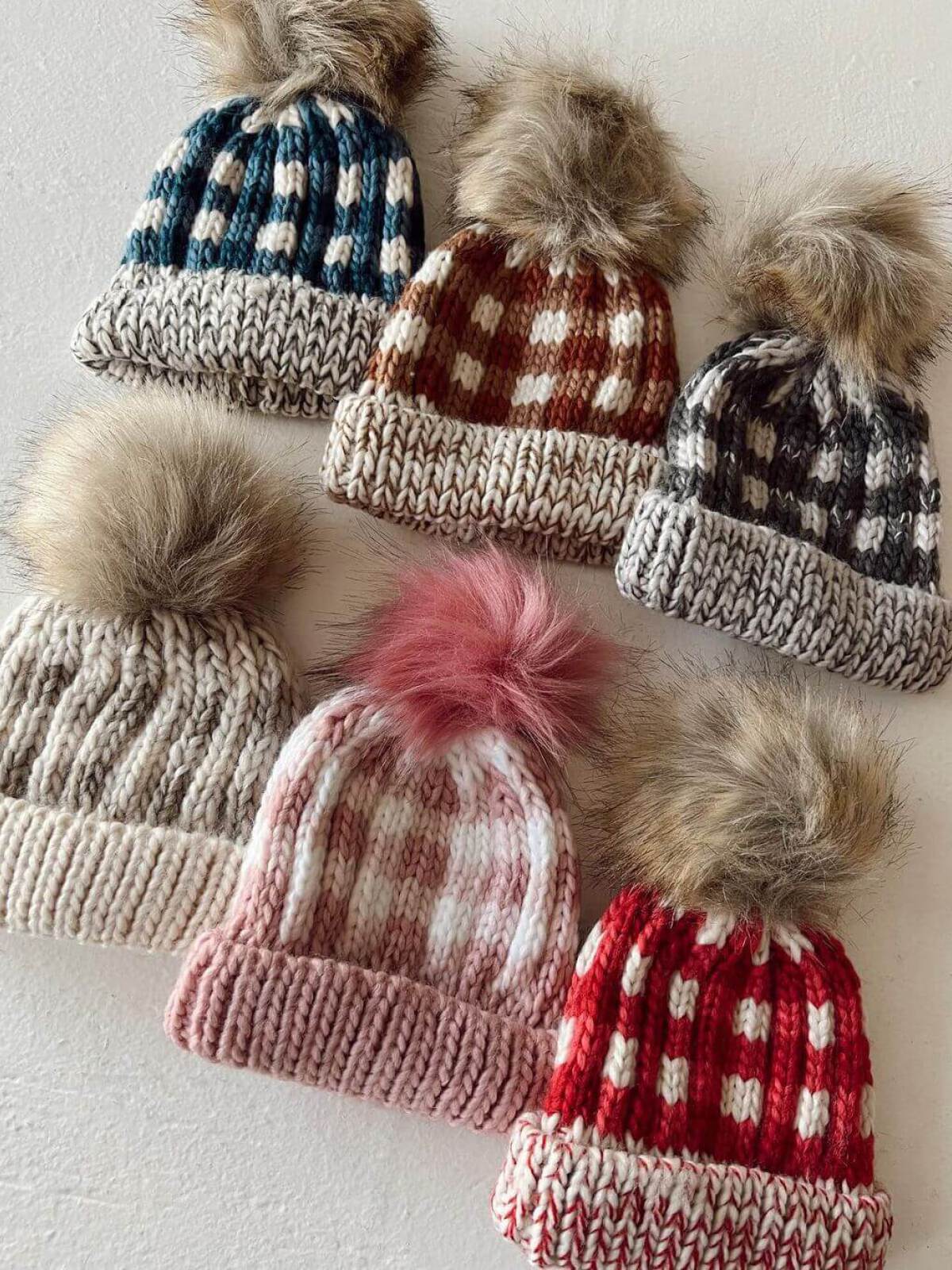 A collection of six knitted winter hats with fur pom-poms in various colors and patterns.
