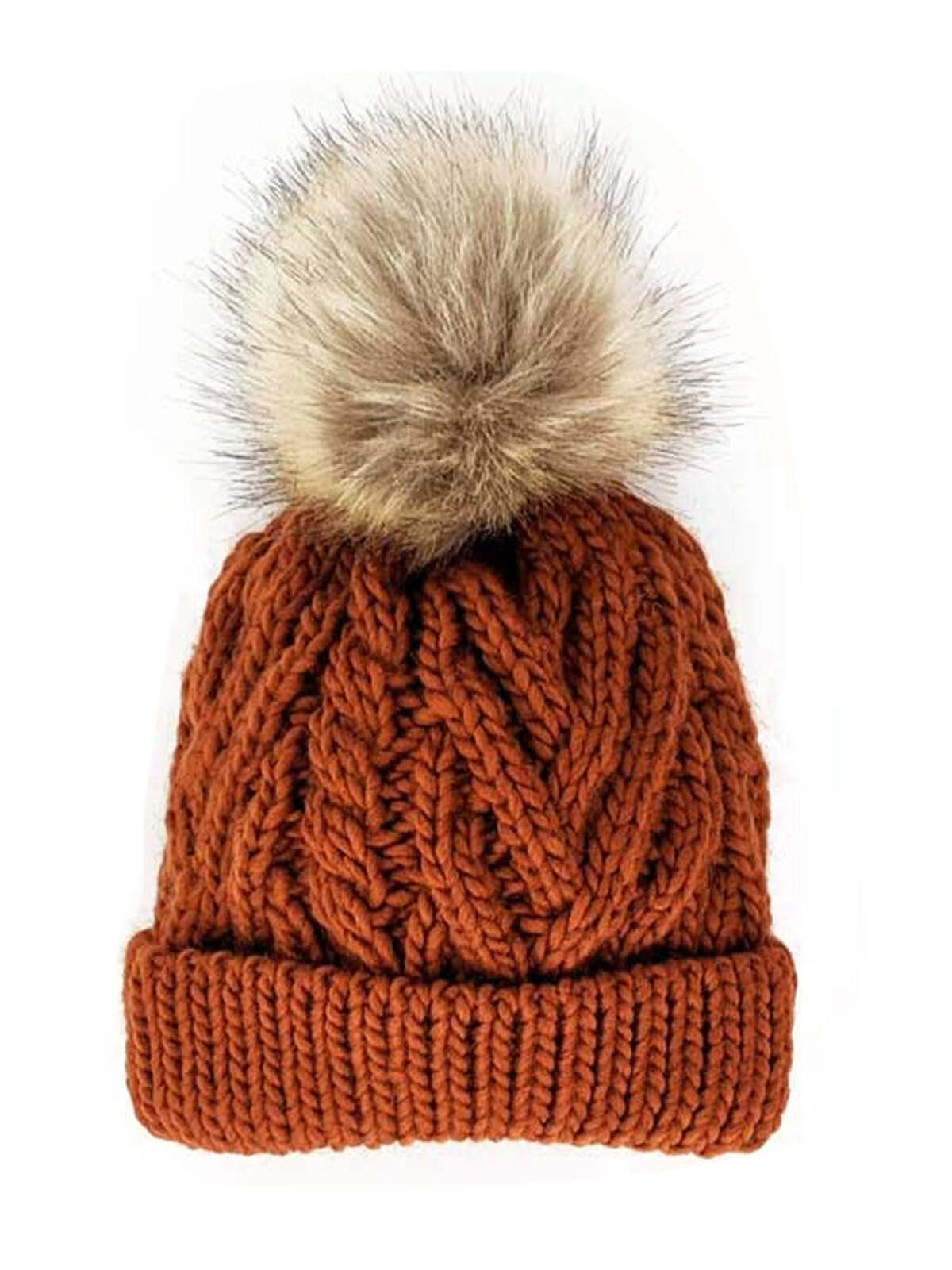 Knitted rust-orange beanie with a plush tan pom-pom on top, featuring a textured cable design.