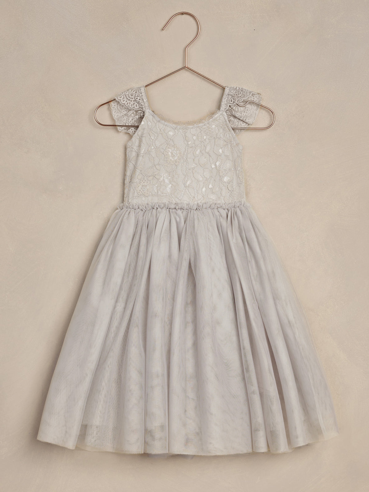 Light gray dress with lace detailing and ruffled sleeves, hanging on a rose gold hanger against a textured background.