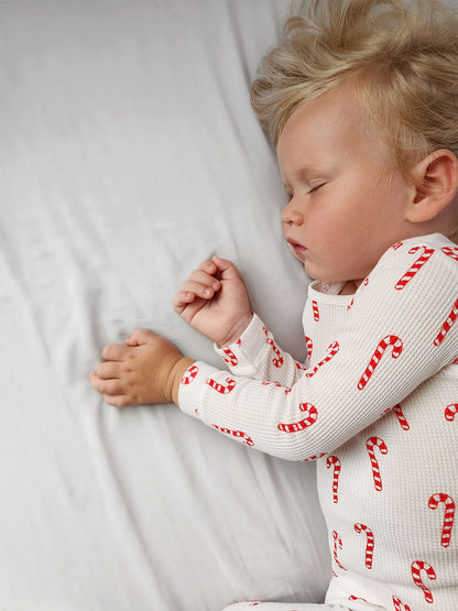 Child sleeping peacefully on a white bed, wearing a candy cane patterned pajama.