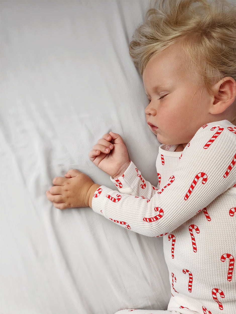 Child sleeping peacefully on a white bed, wearing a candy cane patterned pajama.