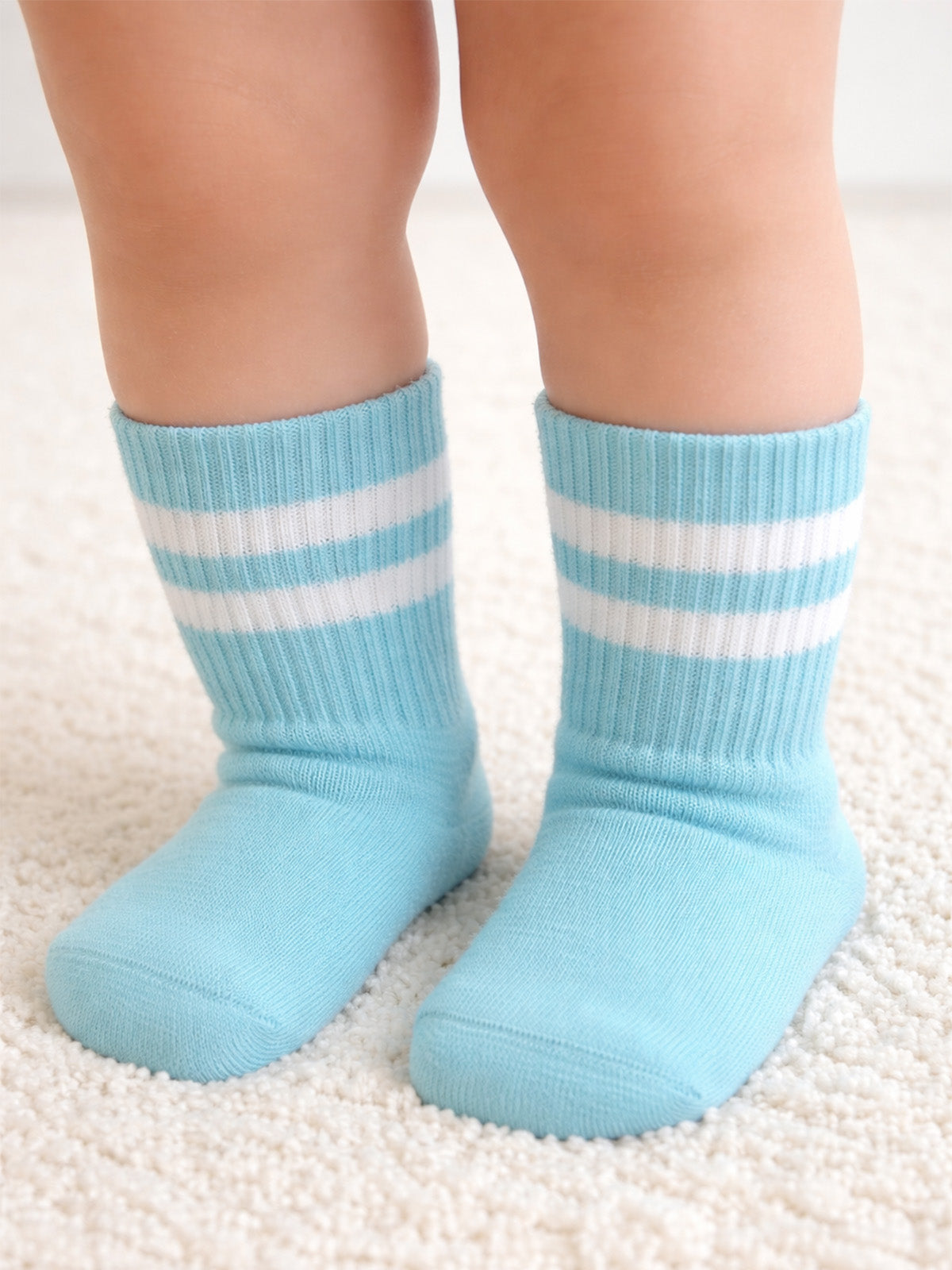 Light blue children's socks with white stripes, resting on a soft, fluffy carpet.