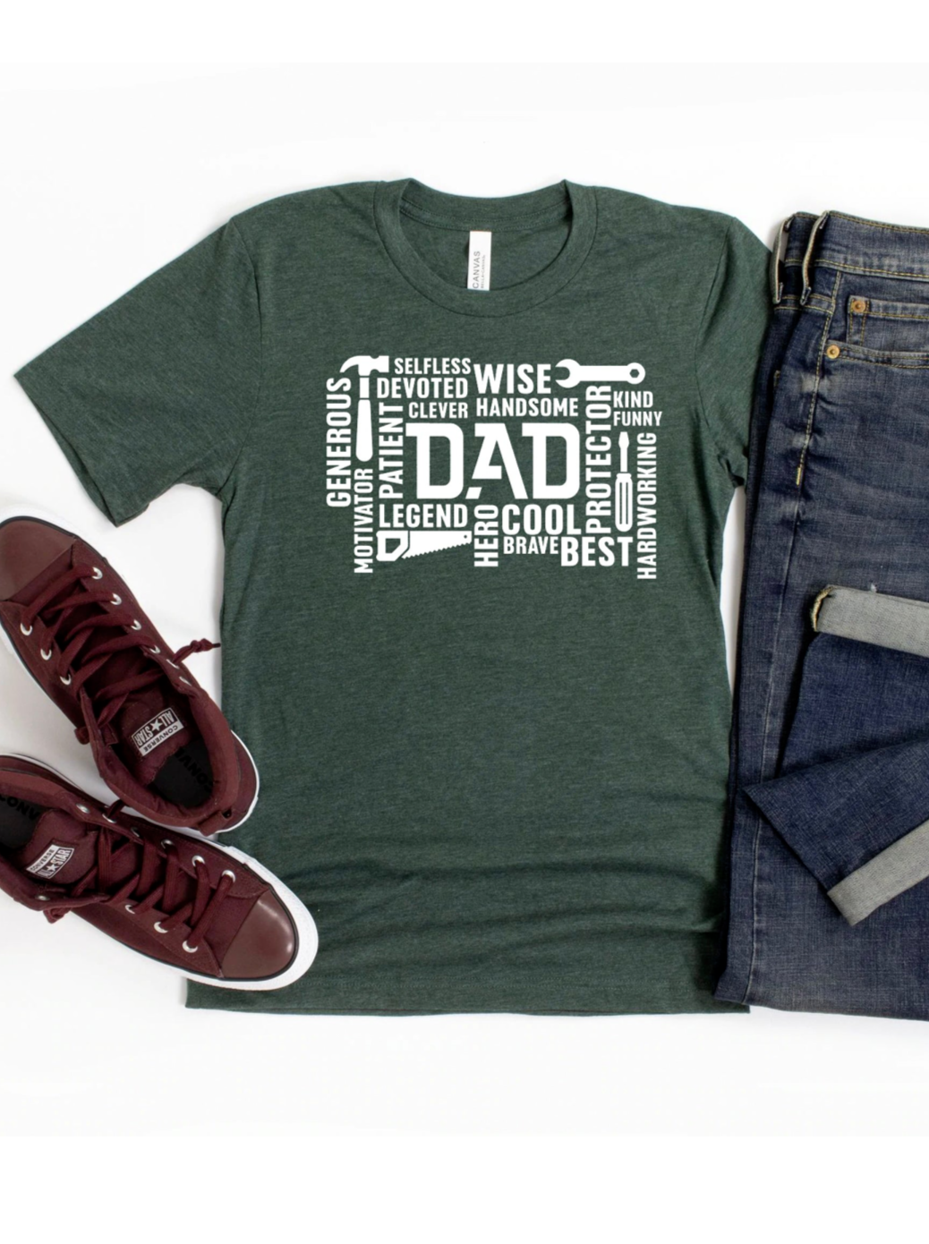 Green t-shirt with "DAD" and descriptive words laid out with jeans and burgundy sneakers.
